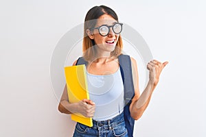 Beautiful redhead student woman wearing a backpack and book pointing and showing with thumb up to the side with happy face smiling