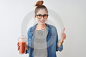 Beautiful redhead woman drinking smoothie of tomato over isolated white background happy with big smile doing ok sign, thumb up