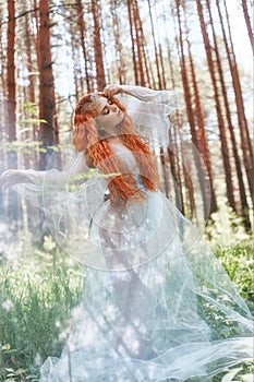 Beautiful redhead woman forest nymph in a blue transparent light dress in the woods spinning in dance. Red hair girls. Art fashion