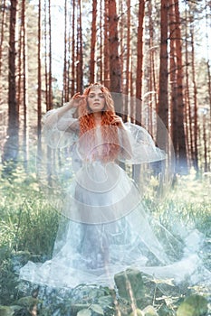 Beautiful redhead woman forest nymph in a blue transparent light dress in the woods spinning in dance. Red hair girls. Art fashion