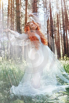 Beautiful redhead woman forest nymph in a blue transparent light dress in the woods spinning in dance. Red hair girls. Art fashion