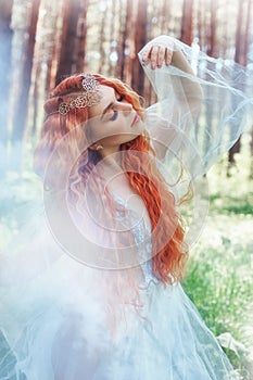 Beautiful redhead woman forest nymph in a blue transparent light dress in the woods spinning in dance. Red hair girls. Art fashion