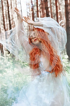 Beautiful redhead woman forest nymph in a blue transparent light dress in the woods spinning in dance. Red hair girls. Art fashion