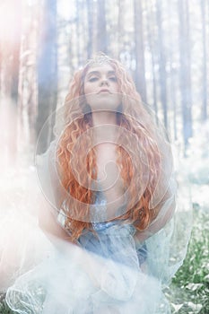 Beautiful redhead woman forest nymph in a blue transparent light dress in the woods spinning in dance. Red hair girls. Art fashion