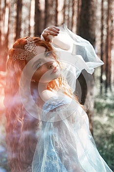 Beautiful redhead woman forest nymph in a blue transparent light dress in the woods spinning in dance. Red hair girls. Art fashion