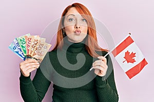 Beautiful redhead woman holding canadian dollars and canada flag looking at the camera blowing a kiss being lovely and sexy