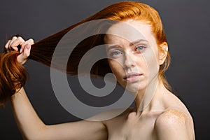 Redhead woman holding her healthy and shiny hair, studio grey