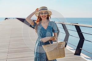 Beautiful redhead woman posing at sunny day. walks along the pier near the sea. Girl wearing fashionable sunglasses blue