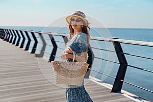 Hermoso pelirrojo una mujer posando sobre el soleado. camina a lo largo de muelle más cercano el mar. agotador de moda gafas de sol azul 