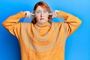 Beautiful redhead woman putting fingers on ears ignoring noise clueless and confused expression