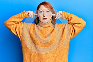 Beautiful redhead woman putting fingers on ears ignoring noise relaxed with serious expression on face