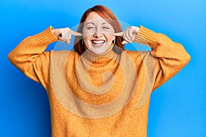 Beautiful redhead woman putting fingers on ears ignoring noise smiling and laughing hard out loud because funny crazy joke