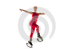 Beautiful redhead woman in a red sportswear jumping in a kangoo jumps shoes isolated on white studio background.