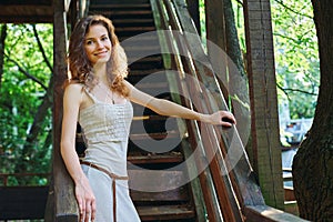 Beautiful redhead woman stands on the wooden stairs of an old house. Smiling young woman in summer dress