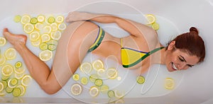 Beautiful redhead woman takes a milk bath with lemon and lime slices. Skin care and whitening. A girl in a yellow green