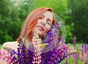 Beautiful redhead woman with vivid lupin bouquet in a field close-up