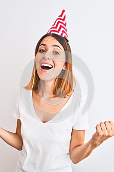 Beautiful redhead woman wearing birthday cap over isolated background celebrating surprised and amazed for success with arms