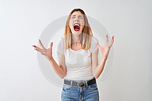 Beautiful redhead woman wearing casual t-shirt standing over isolated white background crazy and mad shouting and yelling with