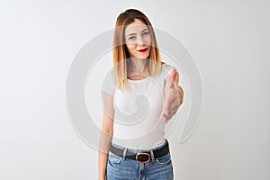 Beautiful redhead woman wearing casual t-shirt standing over isolated white background smiling friendly offering handshake as