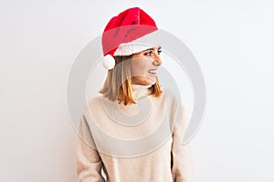 Beautiful redhead woman wearing christmas hat over isolated background looking away to side with smile on face, natural expression
