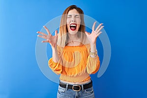 Beautiful redhead woman wearing orange casual t-shirt standing over isolated blue background celebrating mad and crazy for success