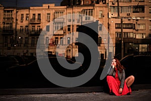 Beautiful redhead woman wearing red dress and stylish coat on city street. loneliness and depression concept