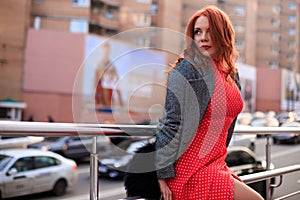 Beautiful redhead woman wearing red dress and stylish coat on city street. loneliness and depression concept