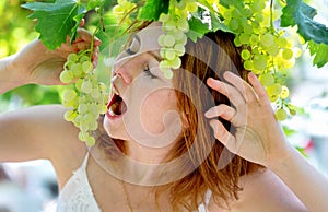 Beautiful redhead woman in white dress is eating green grapes