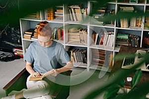 Beautiful redhead young woman student is reading book enjoys of rest at home office.