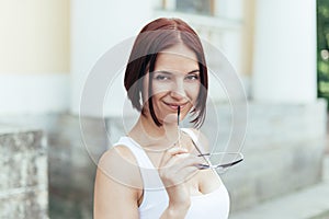 A beautiful redheaded girl smiles cheerfully holding her glasses