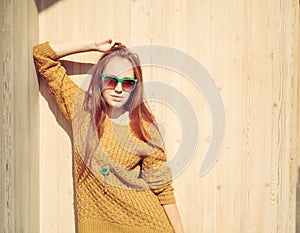 Beautiful redheaded girl in sunglasses standing near wooden wa