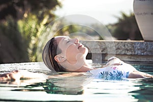 Beautiful relaxed woman in the pool, immersed in the water with her eyes closed. Reflection in the water