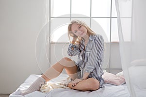 Beautiful relaxed young woman sitting on bed near the window