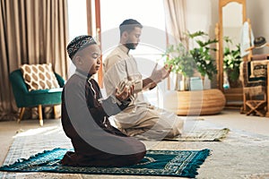 A beautiful religion of brotherhood and devotion. a young muslim man and his son praying in the lounge at home.