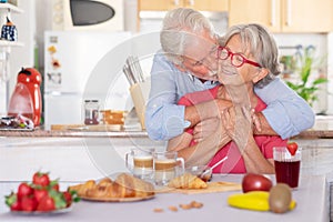 Beautiful retired senior couple having breakfast at home, starting morning with a kiss. Hot cappuccino croissant on the table