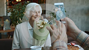 Beautiful retired woman posing for smartphone camera holding flowers in restaurant