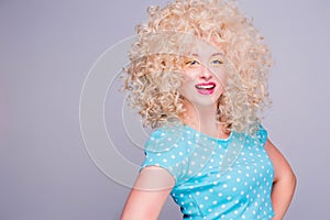 Beautiful retro-style blonde girl with voluminous curly hairstyle, in a blue polka-dot blouse on a gray background, smiles and