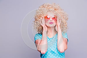 Beautiful retro-style blonde girl with voluminous curly hairstyle, in a blue polka-dot blouse and pink glasses on a gray