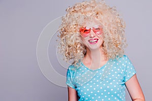 Beautiful retro-style blonde girl with voluminous curly hairstyle, in a blue polka-dot blouse and pink glasses on a gray