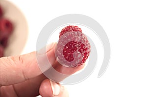 Beautiful ripe raspberries in female fingers on a white background