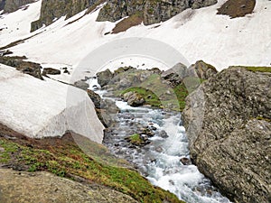 Beautiful river stream flowing in between a huge rock on one side and a snow glacier on other side in an epic Indian Himalayan Val