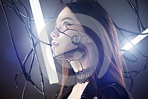 Beautiful robot girl in cyberpunk style looking up on background of wires and glowing lamps