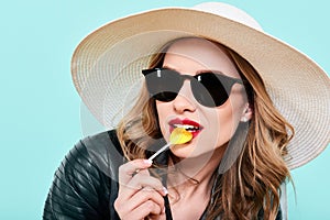 Beautiful rocker girl in leather jacket and sunglasses with heart shaped lollipop. Attractive cool young woman fashion portrait.