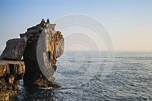 Beautiful rocky cliff landscape with sunset over ocean with undientified people on cliff top