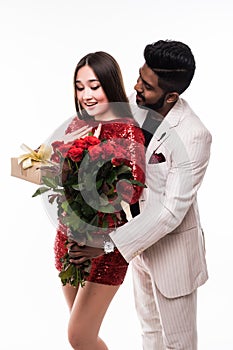 Beautiful romantic asian couple, young asian woman in dress holding red roses and handsome indian man in suit are in love isolated
