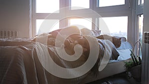 Beautiful romantic brunette woman lying on bed by the window with her lovely cat during amazing sunset