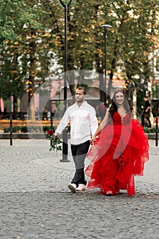 Beautiful romantic couple. Attractive young woman in red dress and crown with handsome man in white shirt with red rose