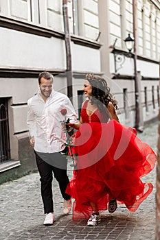 Beautiful romantic couple. Attractive young woman in red dress and crown with handsome man in white shirt with red rose
