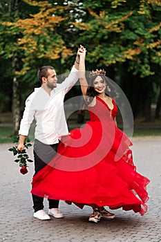 Beautiful romantic couple. Attractive young woman in red dress and crown with handsome man in white shirt with red rose