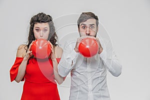 Beautiful romantic couple isolated on white background. An attractive young woman and her husband inflate the balloons